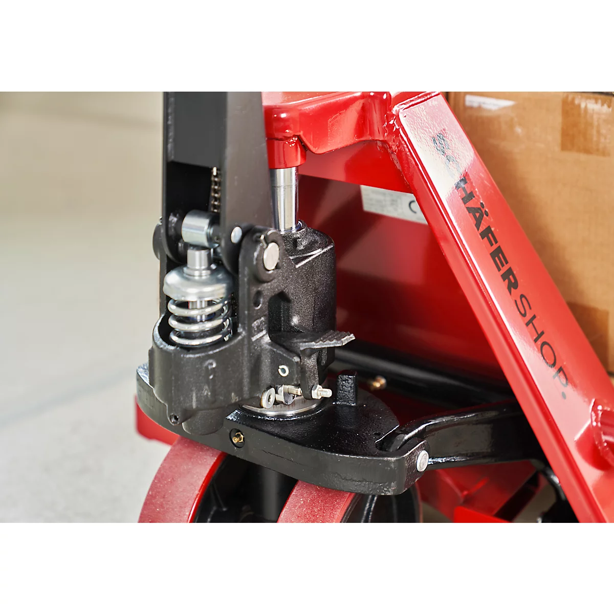 Detailaufnahme einer roten und schwarzen Palettenhubwagen-Mechanik. Häfershop ist auf der Seite zu lesen.