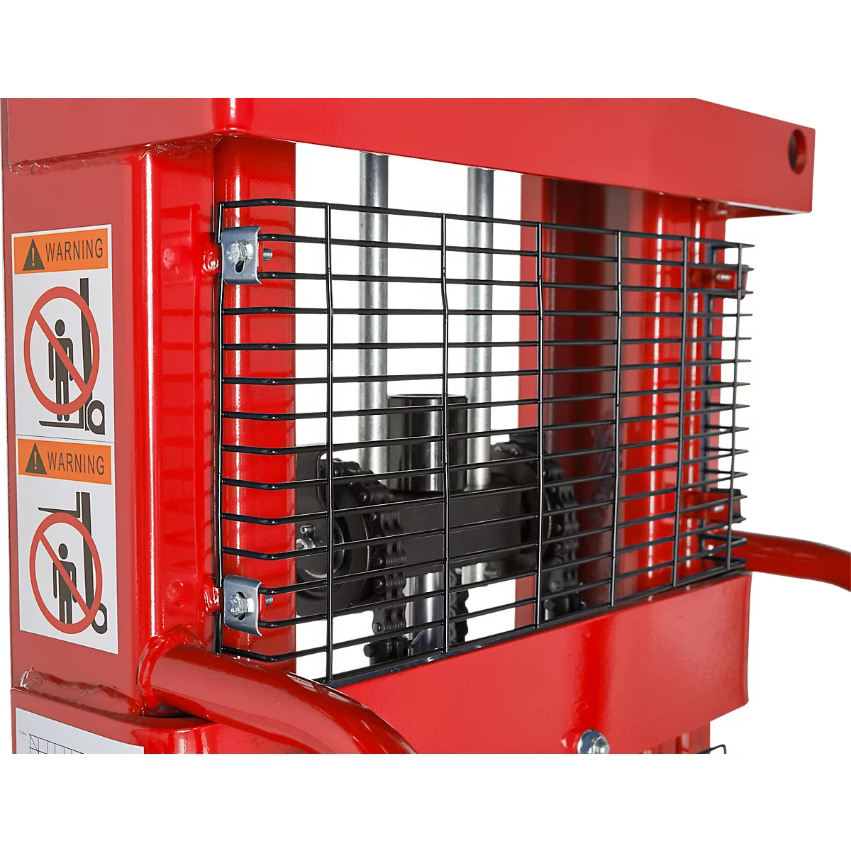 Detail of a red machine with a black protective grille, in front of which are two warning signs with pictograms.