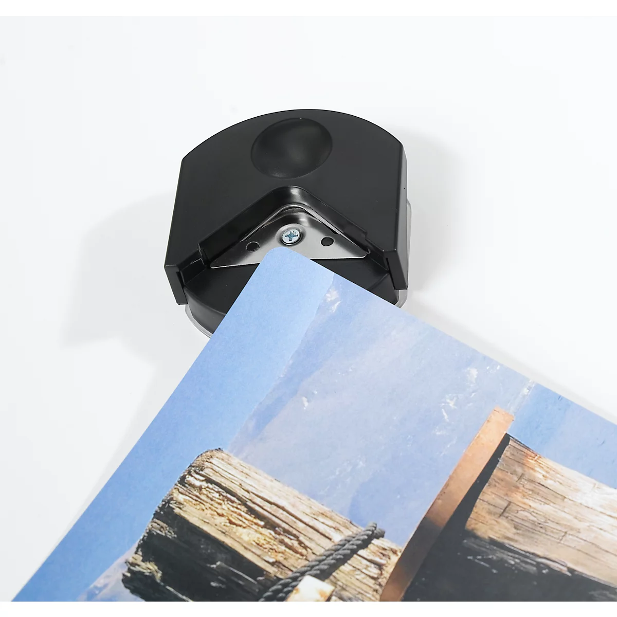 Black plastic corner rounder cutting off a printed sheet of paper. The background is white.