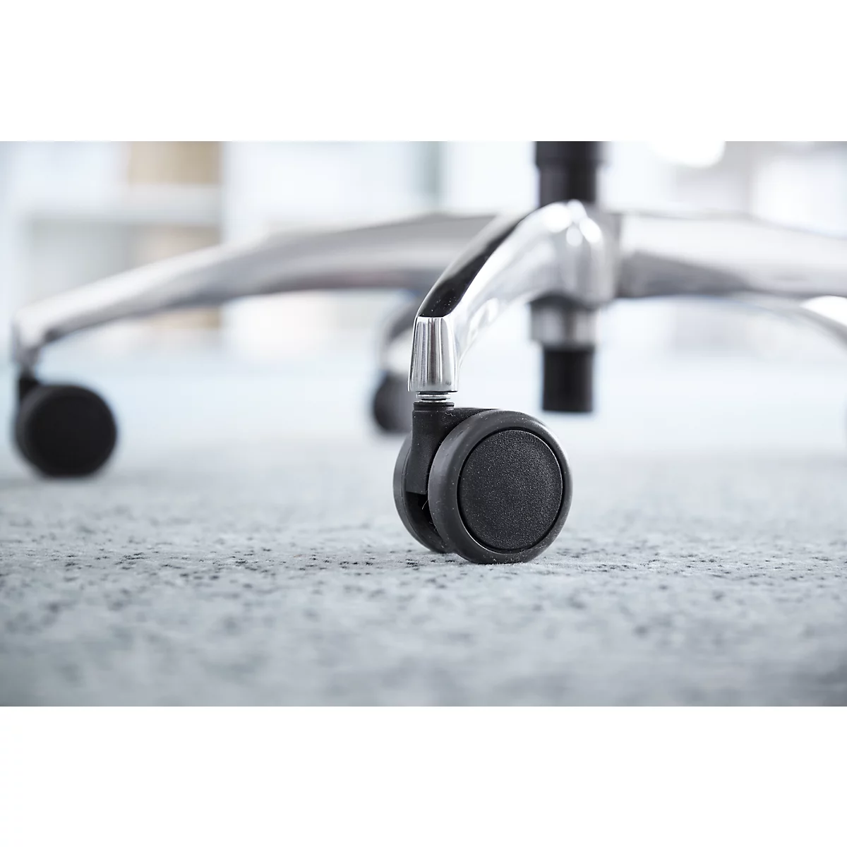 Close-up of a chair on a carpet, focus on a black wheel.