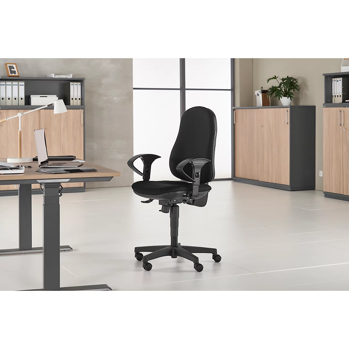 Black office chair in front of a desk, grey cabinets, and a window.