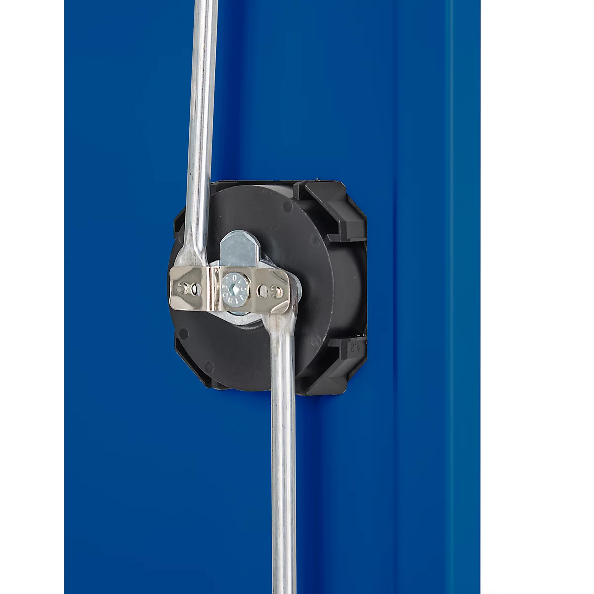 Nahaufnahme eines Metallmechanismus an einer blauen Oberfläche. Ein schwarzes, sechseckiges Gehäuse umschließt Teile aus silberfarbenem Metall.