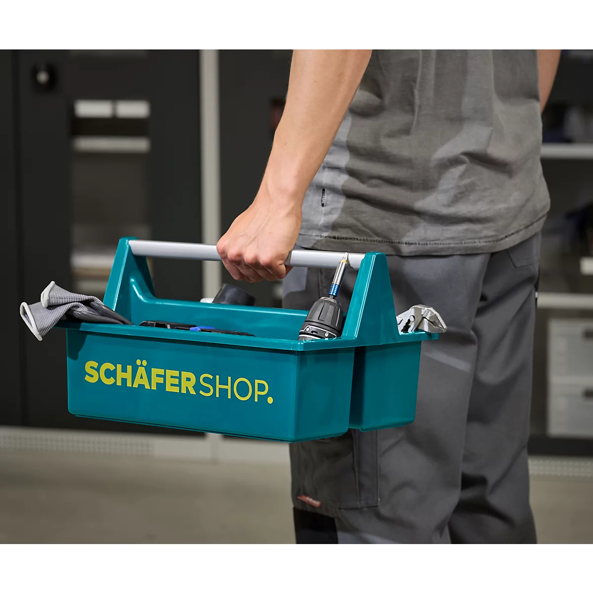 Person trägt eine grüne Werkzeugkiste mit dem Schriftzug SCHÄFER SHOP; Werkzeug liegt darin.