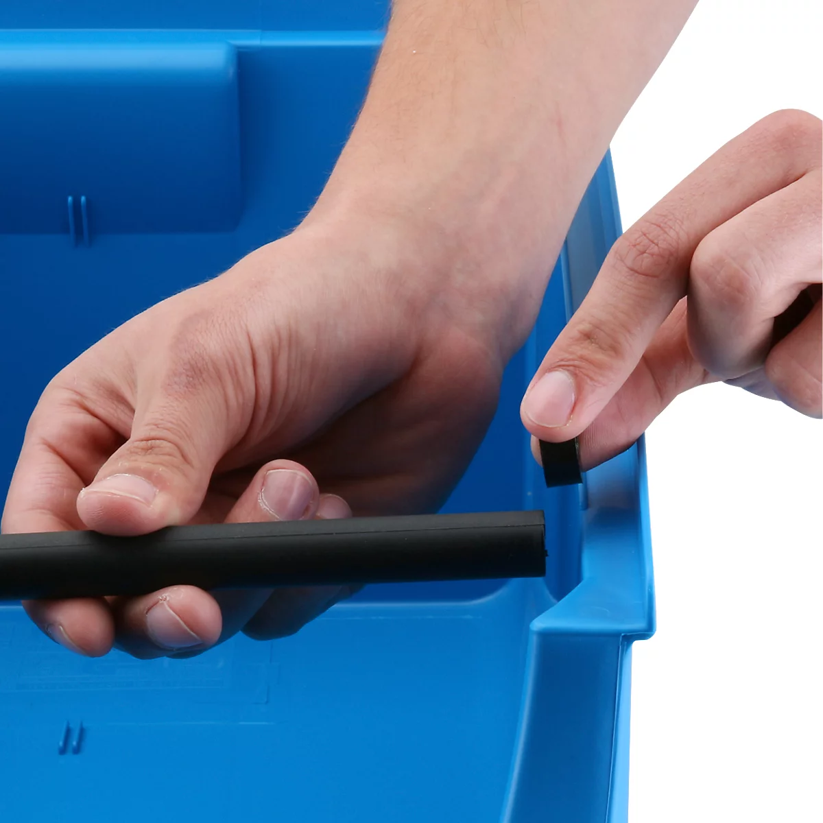 Hände setzen eine schwarze Stange in eine blaue Kunststoffbox ein.