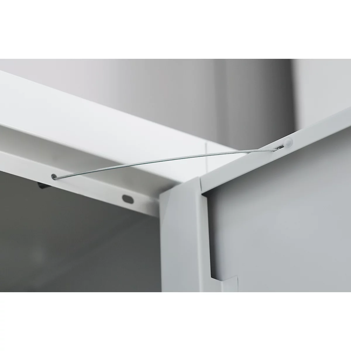 Detail of a cabinet corner joint. A wire spans between two white metal parts.