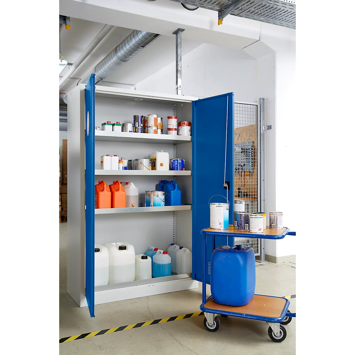 Une armoire bleue ouverte avec divers contenants et pots de peinture. À côté, un chariot avec des seaux de peinture et un tonneau bleu.