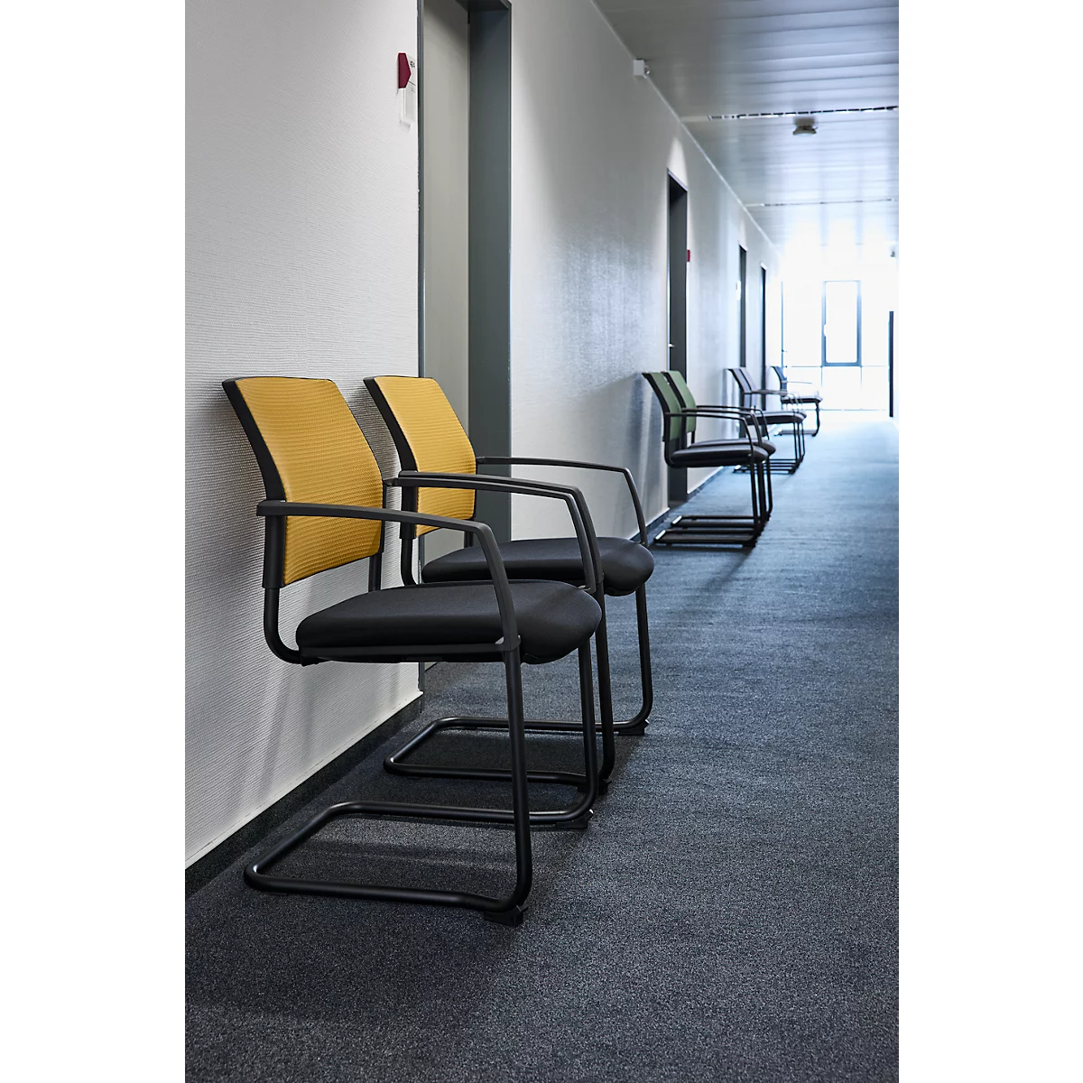Reihe schwarzer Stühle mit gelben Rückenlehnen in einem Gang.