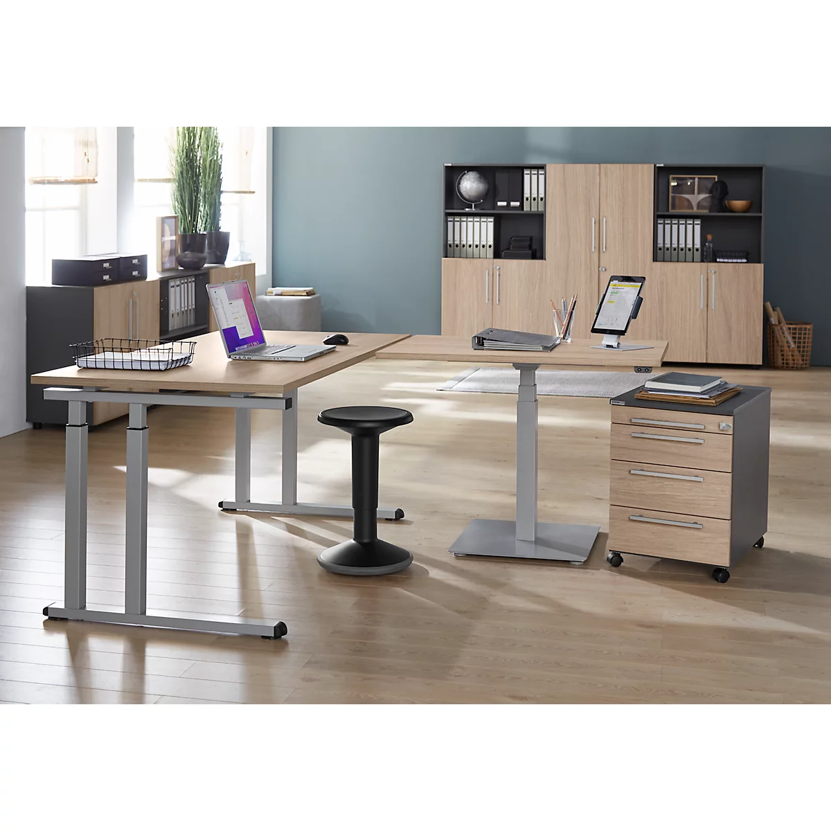 Bureau avec bureaux réglables en hauteur, chaise, caisson mobile et placards. Ordinateurs portables et tablettes sur les bureaux.