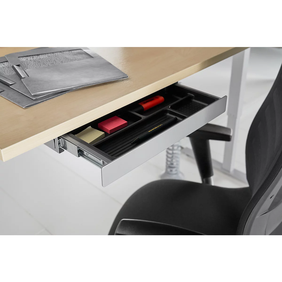 Bureau avec tiroir rempli de fournitures de bureau, stylos, post-it et un marqueur rouge.