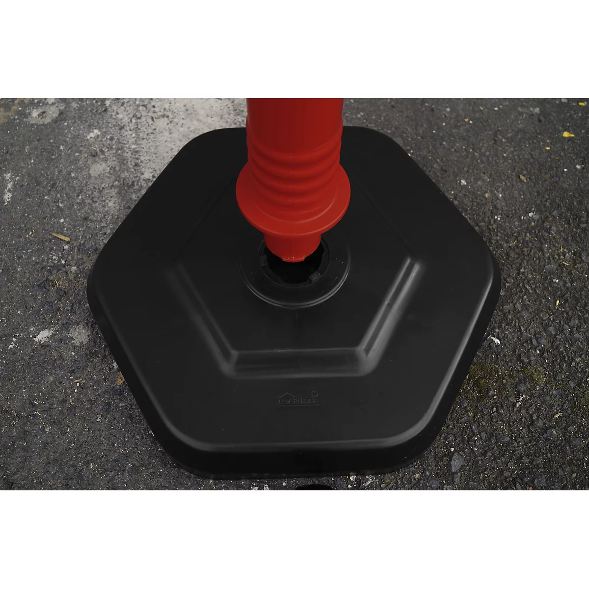 Black hexagonal base of a red-orange marker post, on a grey surface.