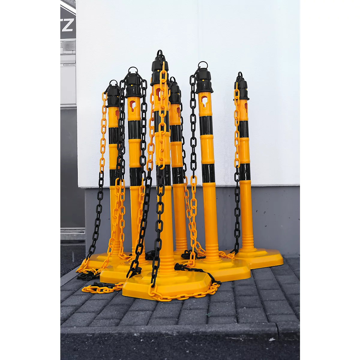 Yellow and black barrier posts with chains on gray pavement, with a white wall in the background.