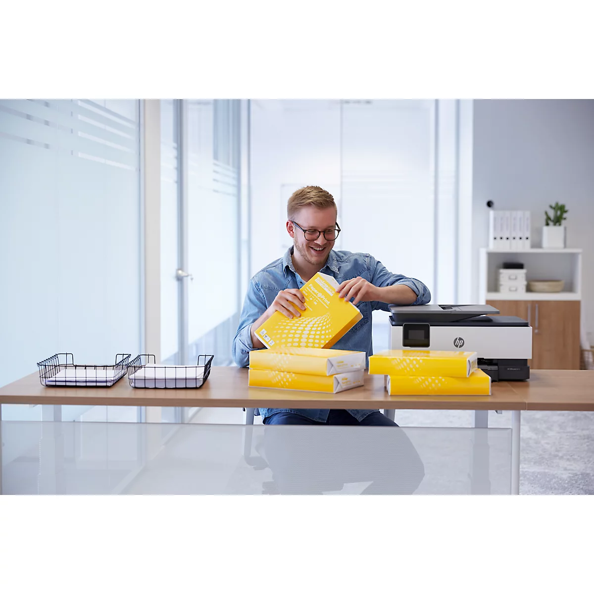 A man with glasses opens a package of yellow paper on a desk.