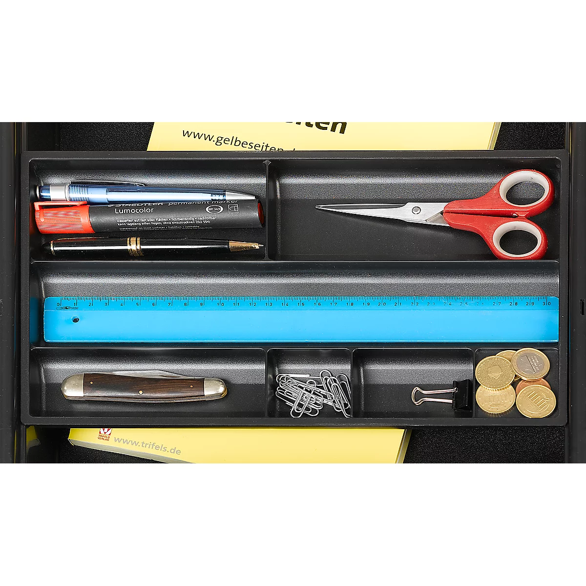 Black drawer filled with stationery: pens, scissors, ruler, coins, paper clips. Yellow note with text.