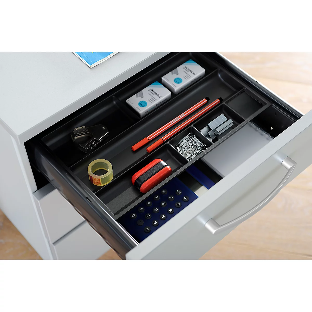 Drawer filled with office supplies, pens, stapler, paper clips and tape.