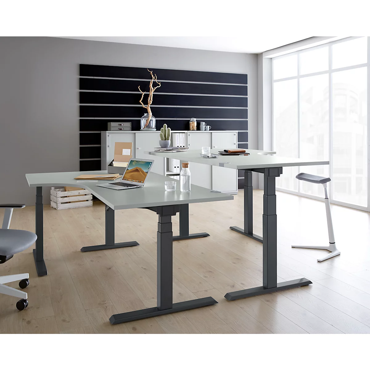 Office with height-adjustable tables, laptop, chair, and decorations. Bright, modern design.
