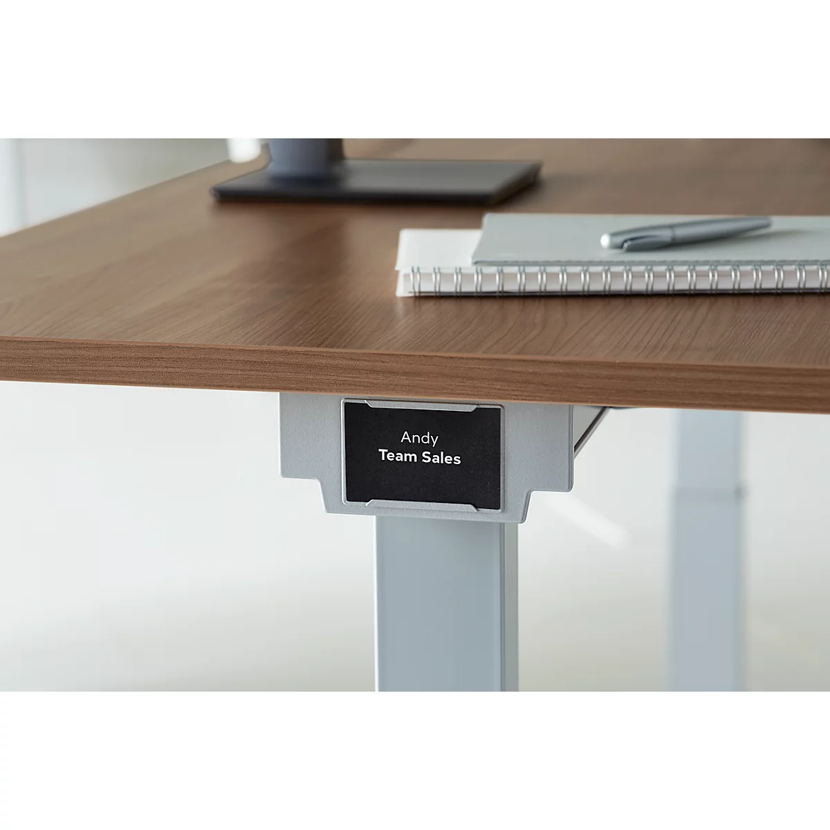 Close-up of a desk with a name plate that reads: Andy, Team Sales. On the desk are a notepad and a pen.