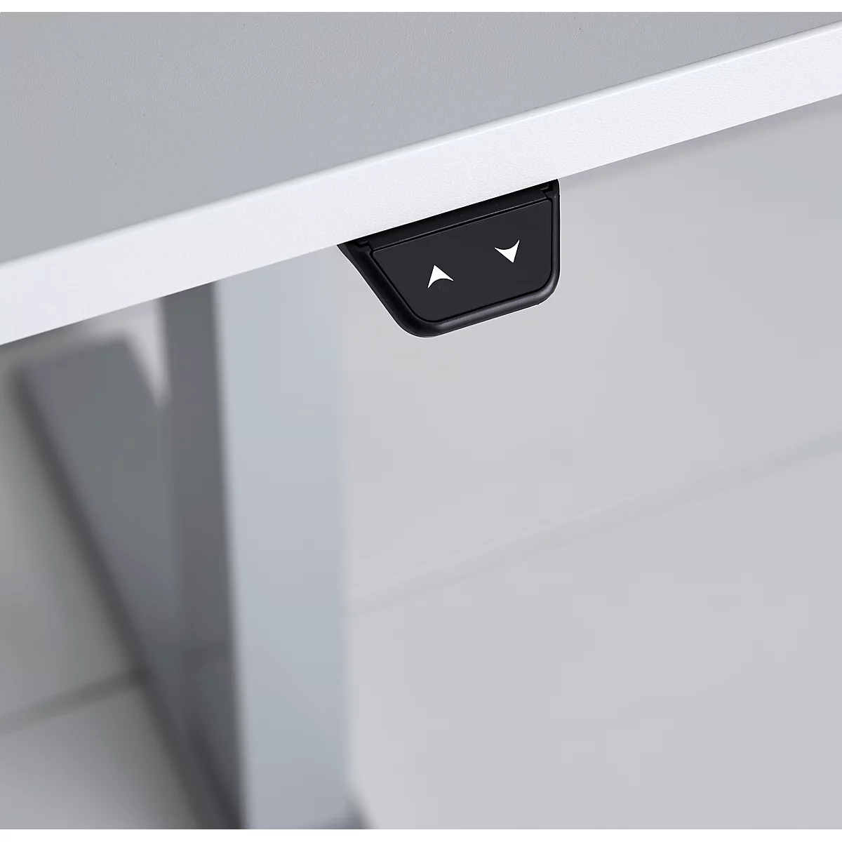 Black control panel with arrow buttons on a white desk edge. The arrows point up and down.