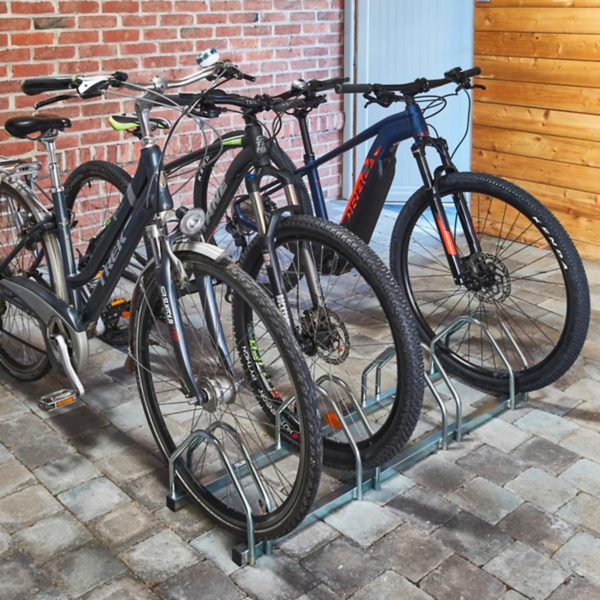 Mehrere Fahrräder stehen in einem Metall-Fahrradständer vor einer Ziegelsteinmauer.