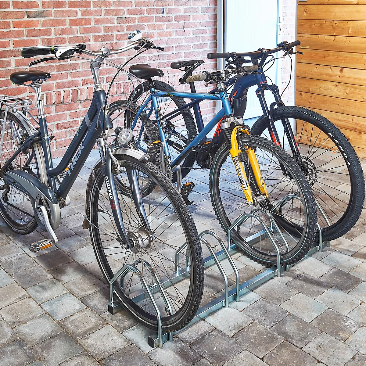 Fahrräder in einem Fahrradständer, vor einer Ziegelwand.
