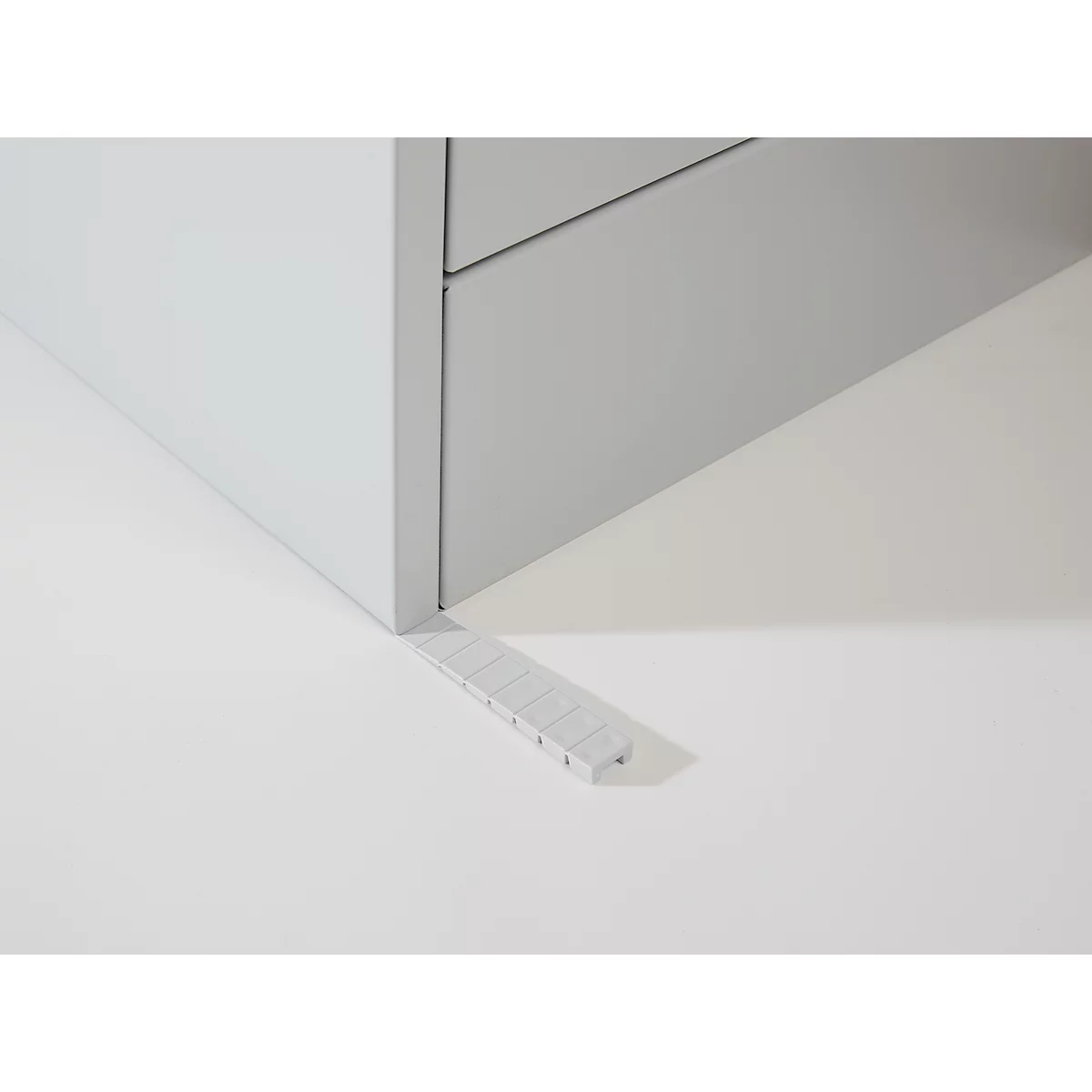 A gray cabinet foot with wedge. The wedge is positioned at an angle under the cabinet foot.