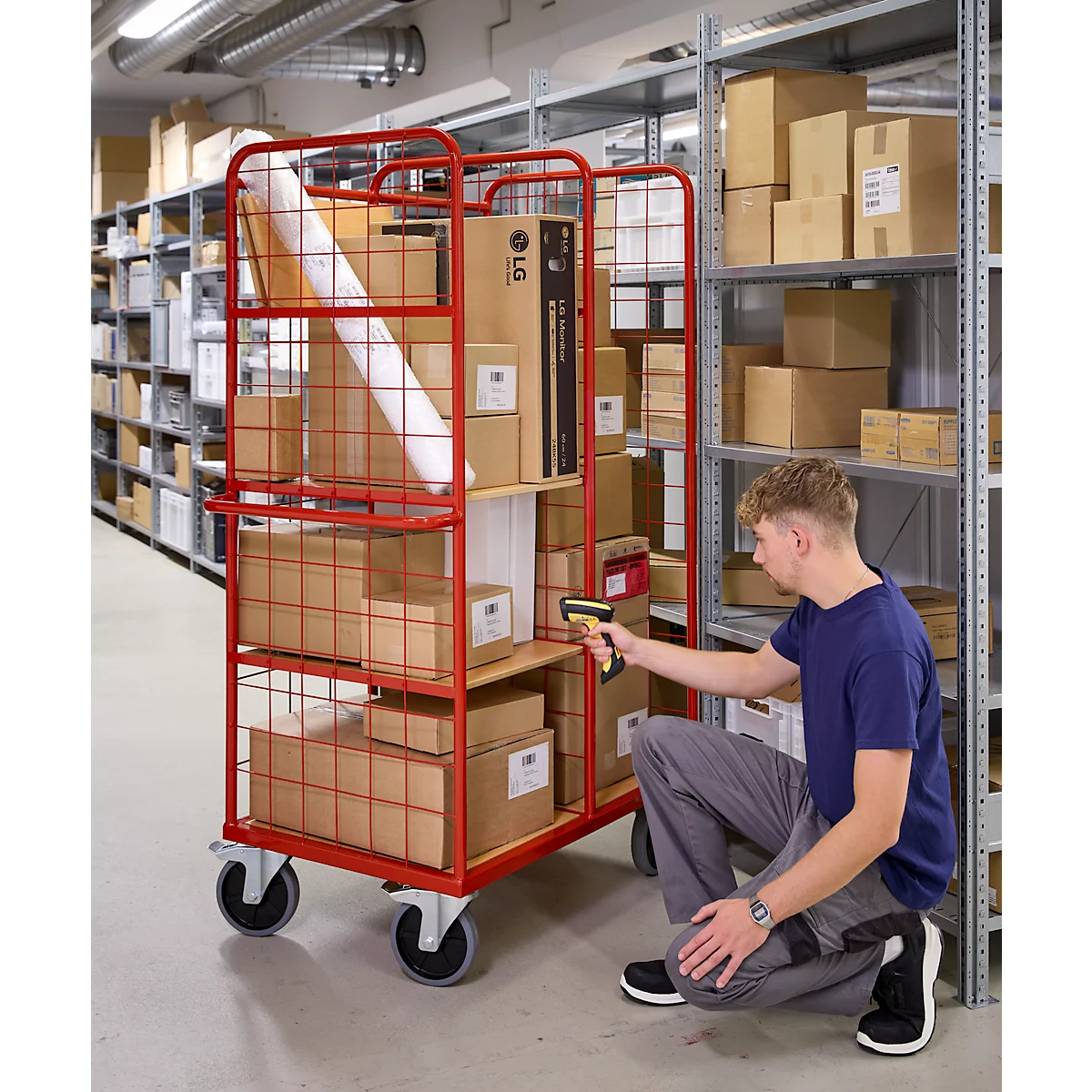Ein Mann scannt Pakete in einem roten Rollwagen, umgeben von Kartons und Regalen in einem Lager.