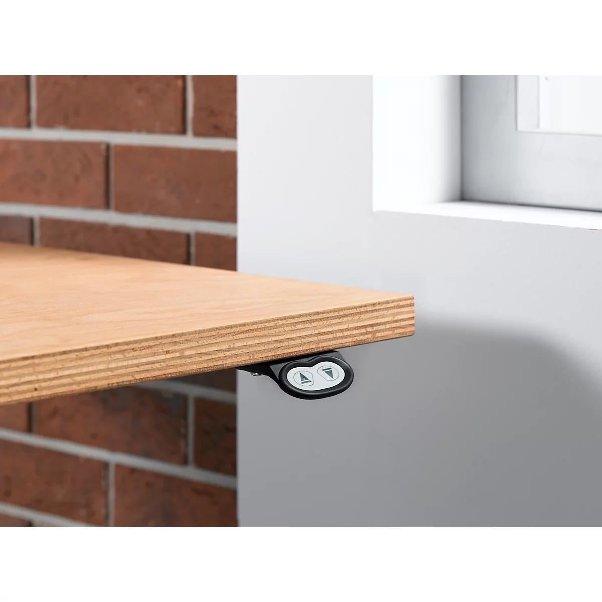 Close-up of a table top with control panel for height adjustment. The table is attached to a brick wall and a white wall.