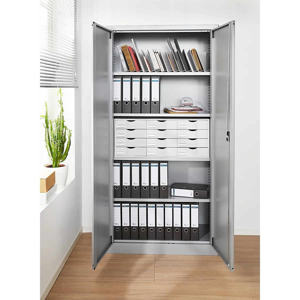 Open gray file cabinet with folders, drawers and books. On light wooden floor.