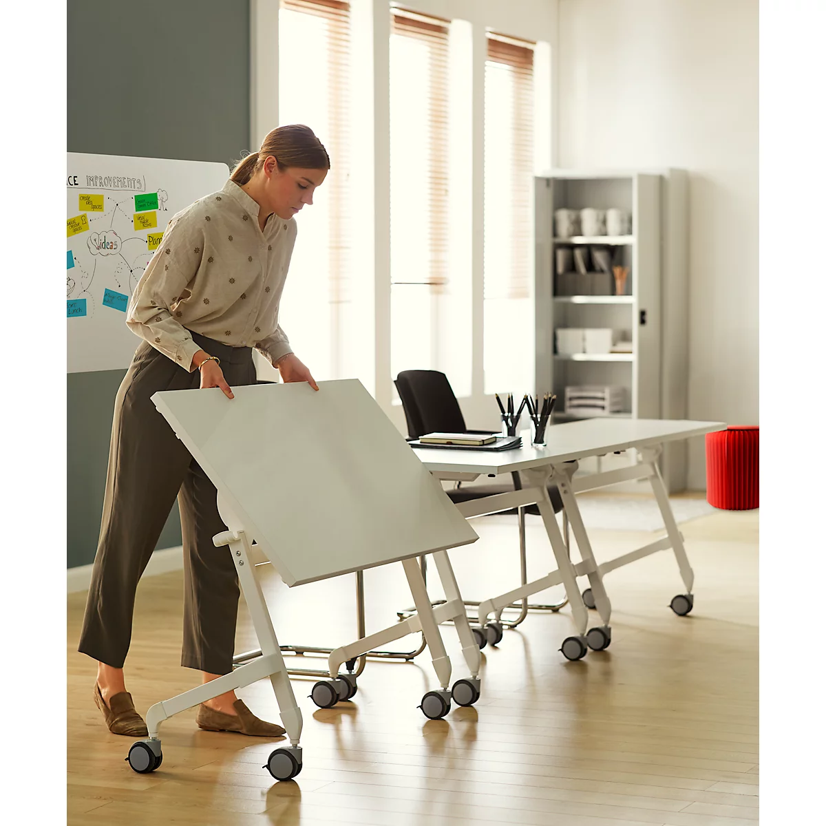 Een vrouw vouwt een witte verrijdbare klaptafel in een modern licht kantoor.