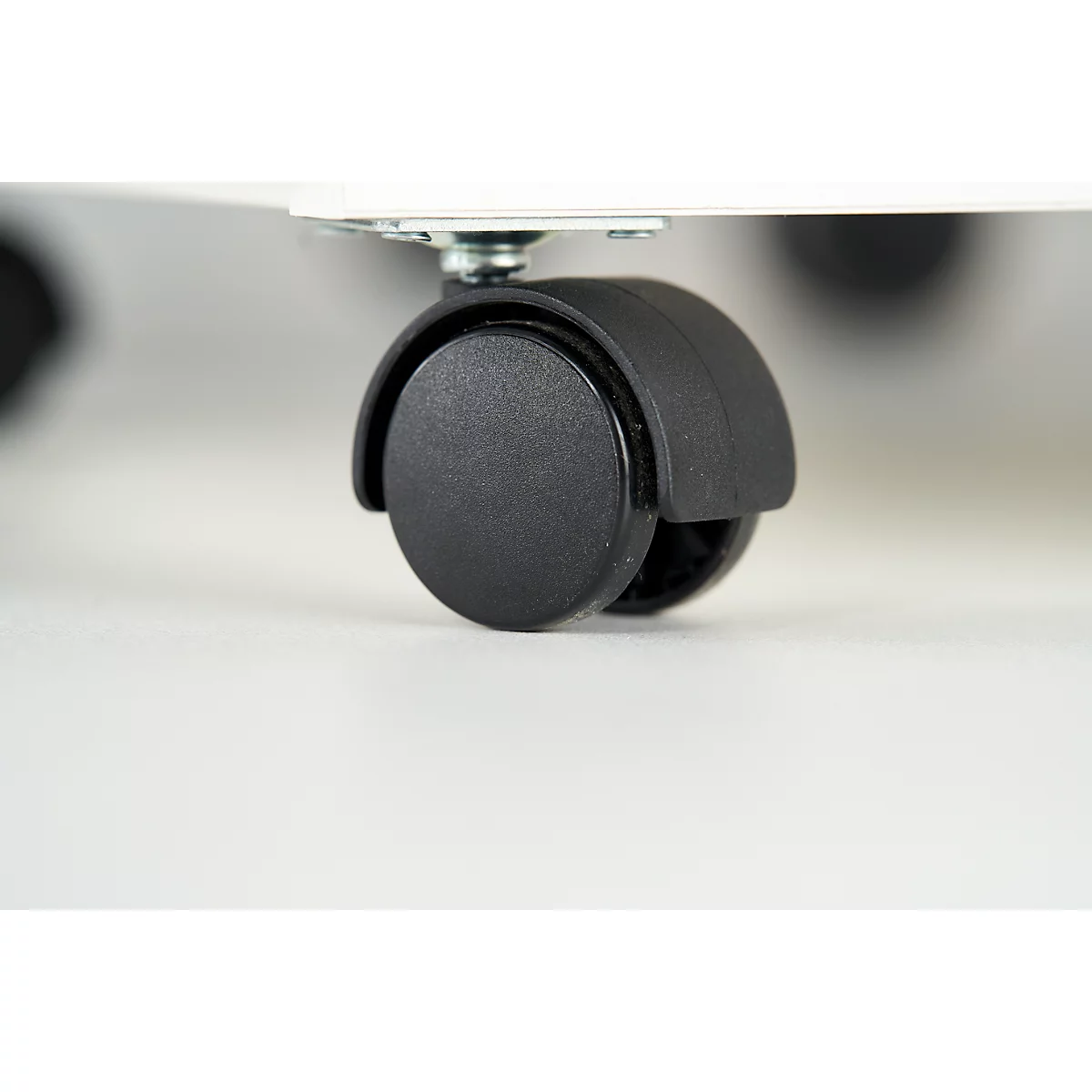 Close-up of a black caster wheel with a silver-colored fixing element on a white surface.