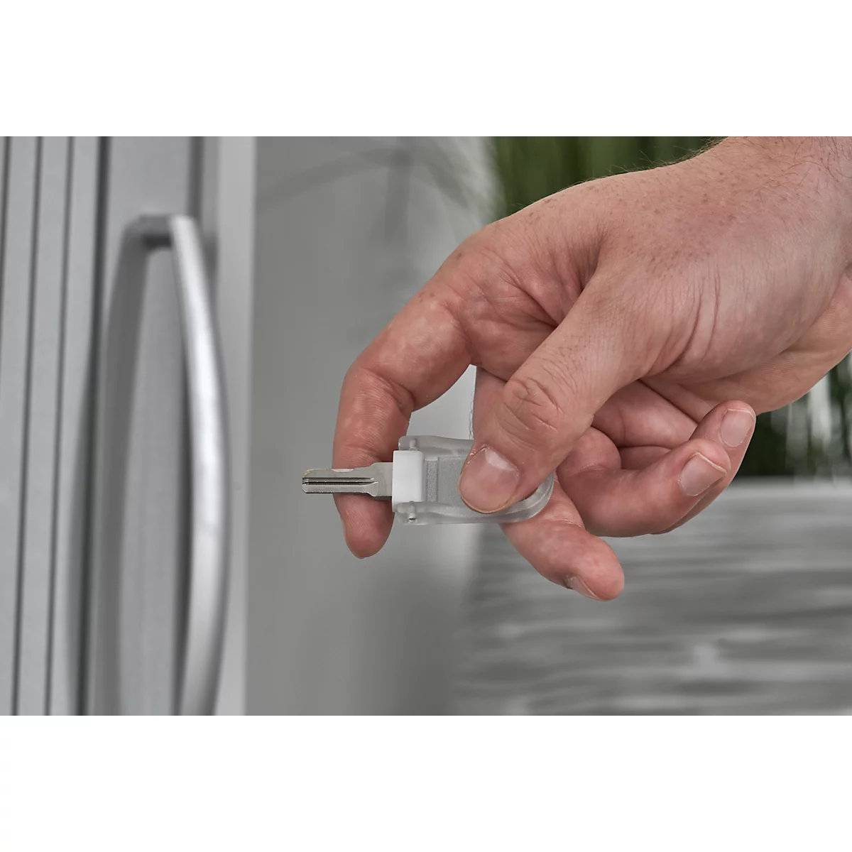 A hand holding a key in front of a door. The key is in a transparent case.