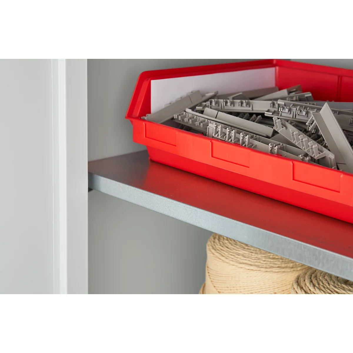 Red plastic box filled with gray components on a shelf. Below, a ball of twine.