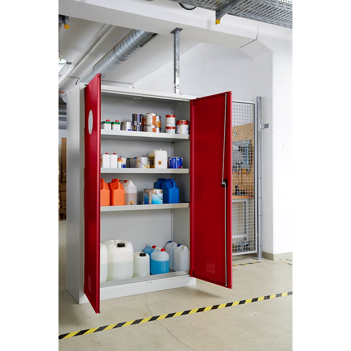 Een rode, open veiligheidskast vol chemische containers en flessen. De kast staat in een magazijn met een gestreepte vloer.