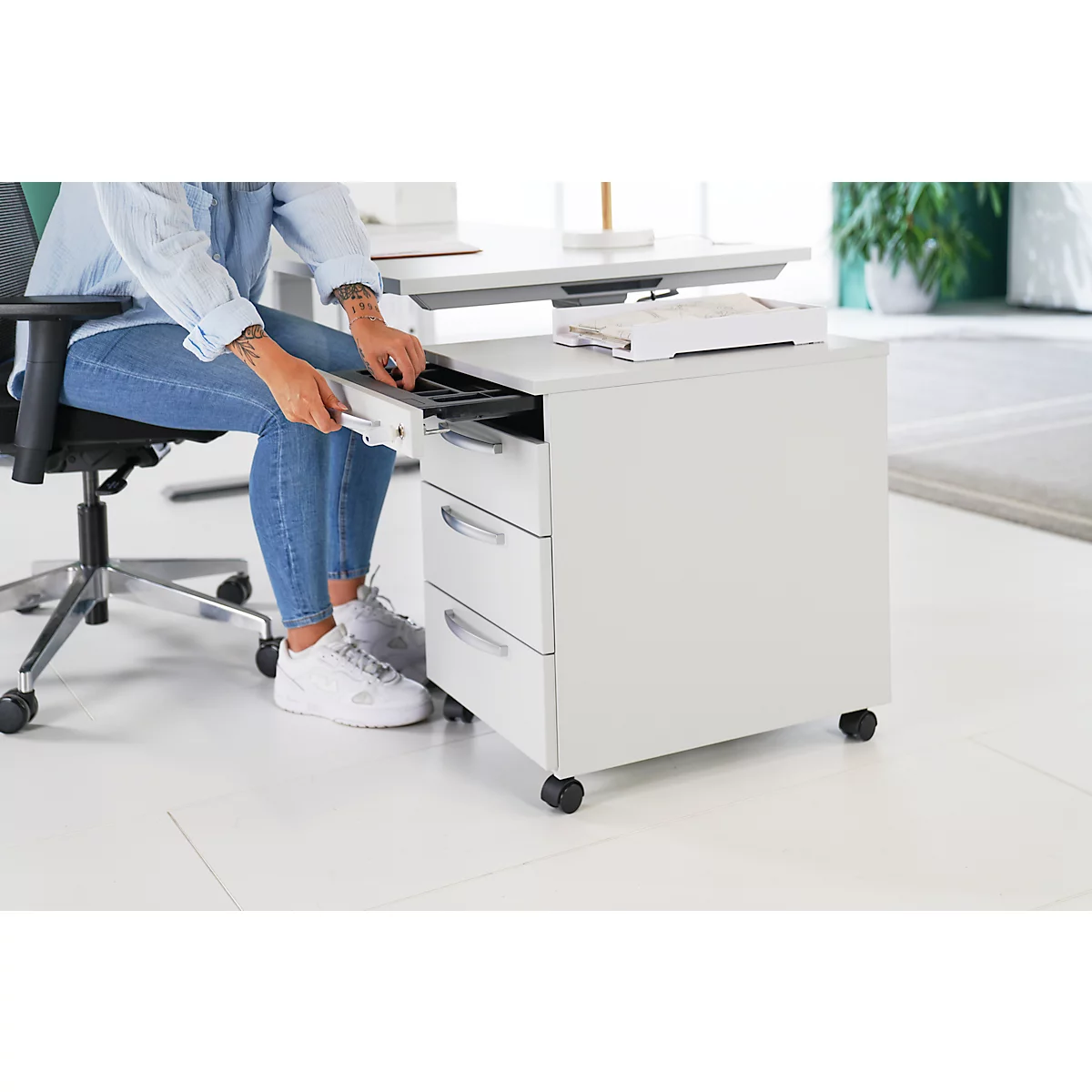 Person opens a drawer on a white mobile pedestal. She is sitting on an office chair.