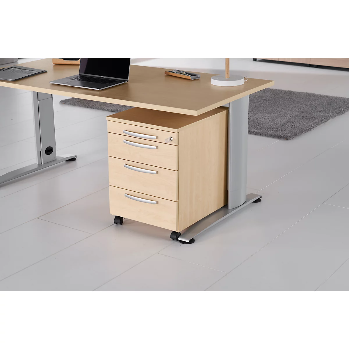 Desk with drawers, laptop and lamp. The cabinet is on wheels.