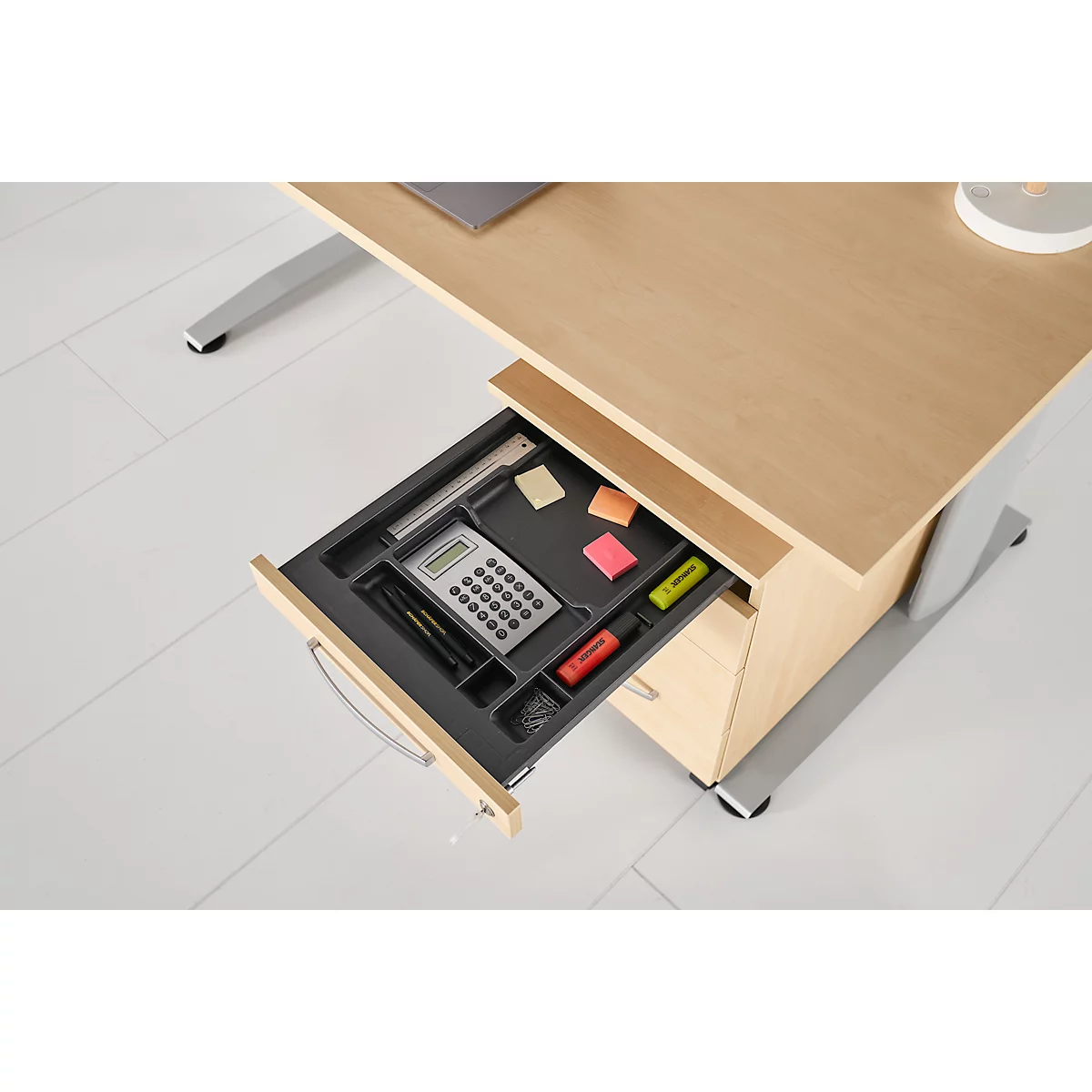 Desk with drawer pulled out. The drawer contains a calculator, pens, sticky notes and highlighters.