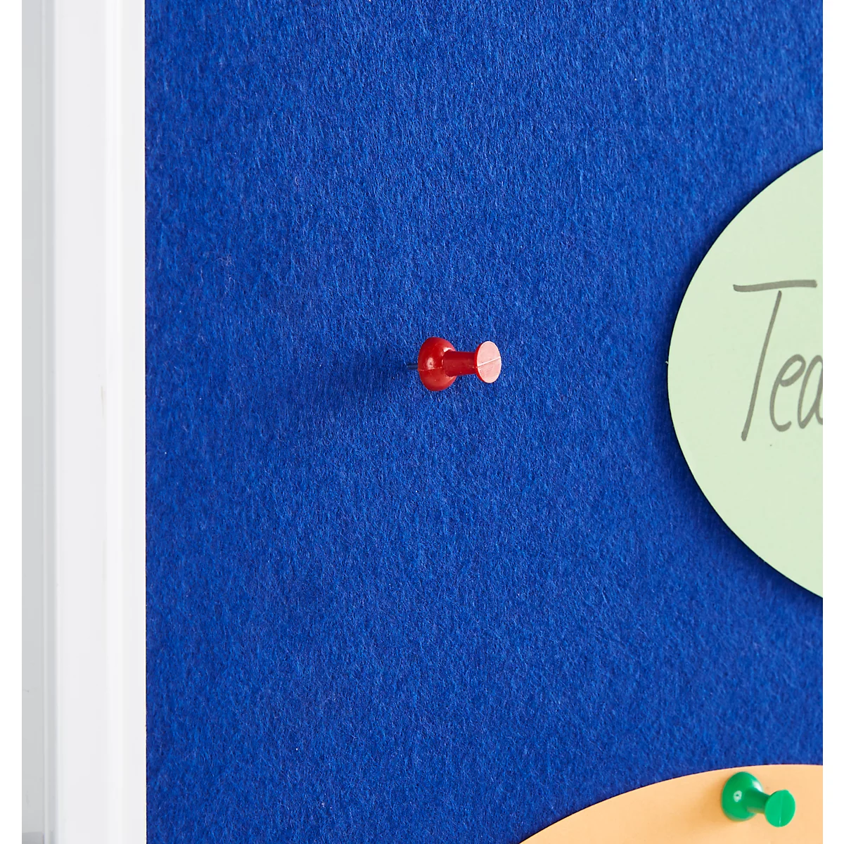 A red pushpin is in a blue felt board, next to a green card with writing.