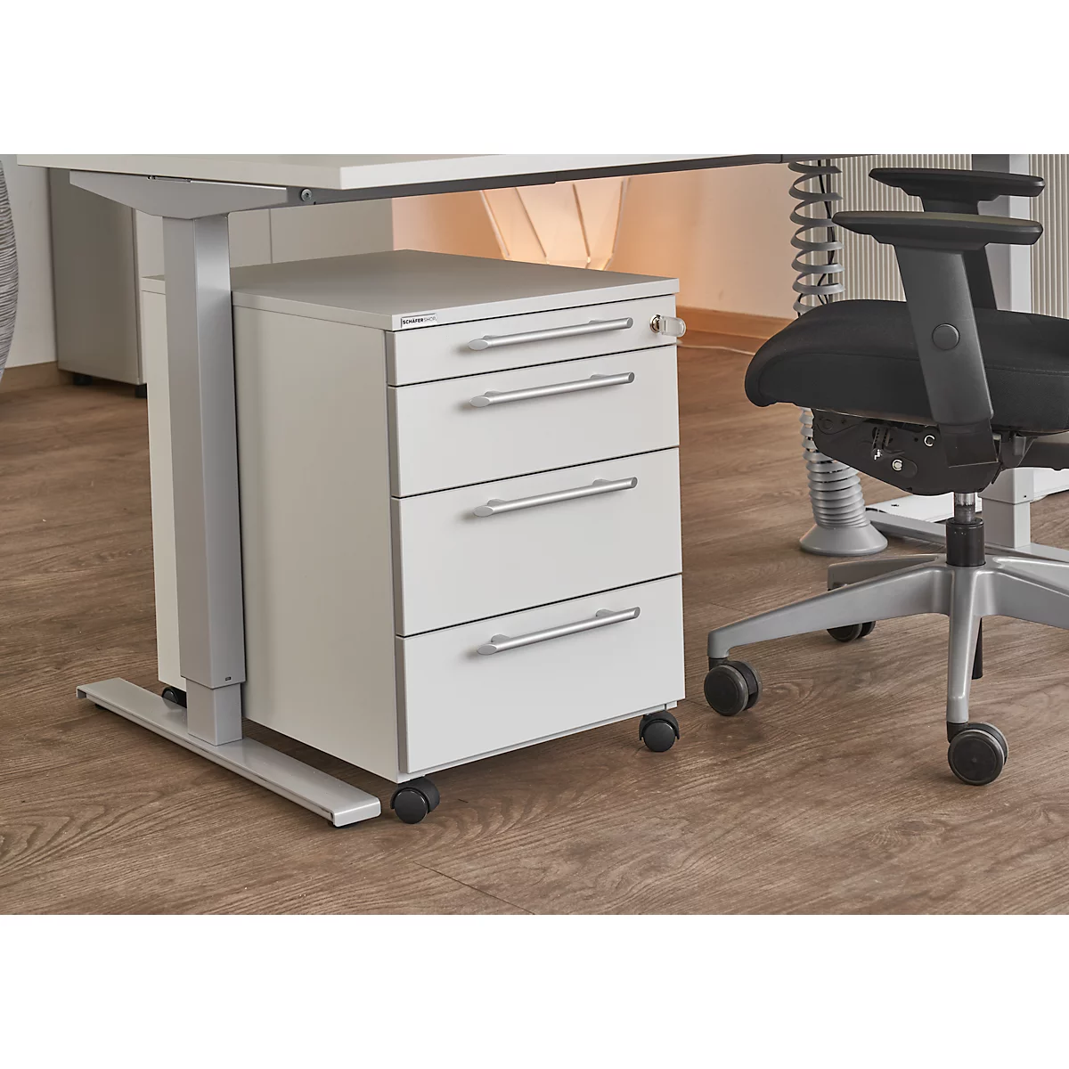 White mobile pedestal with four drawers under a desk. To the right, an office chair. Gray-silver details.