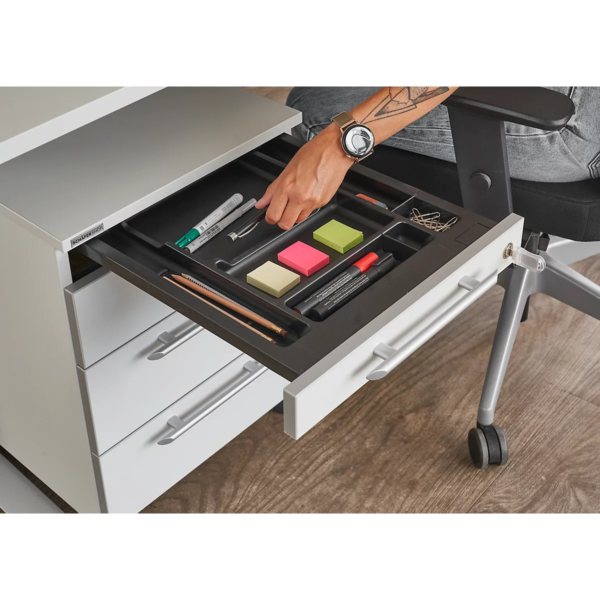 Person opens drawer of white desk container. The drawer contains pens, sticky notes and paper clips.