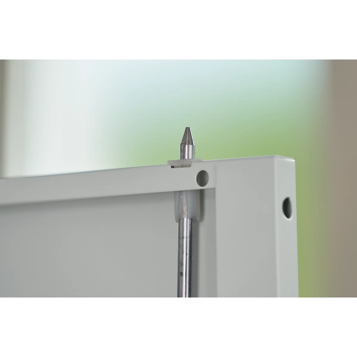 Detailopname van een metalen pin bevestigd aan een metalen beugel. De achtergrond is onscherp, met tinten groen en beige.