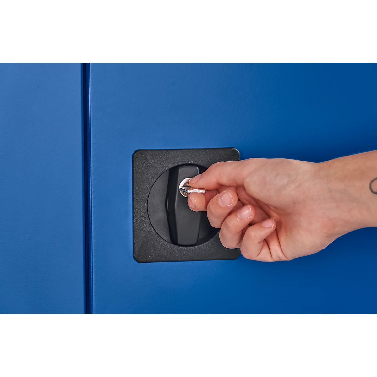 Close-up van een hand die een sleutel in een blauw slot steekt. Een kleine tatoeage is zichtbaar op de pols.