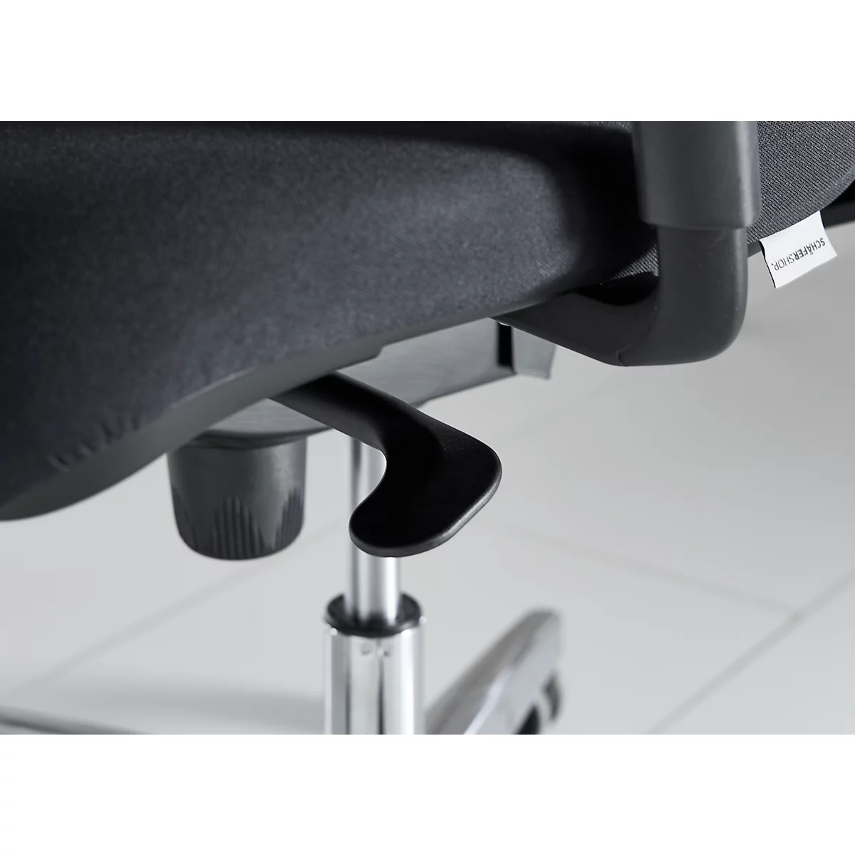 Close-up of a black office chair: lever, seat and base. Label with lettering.