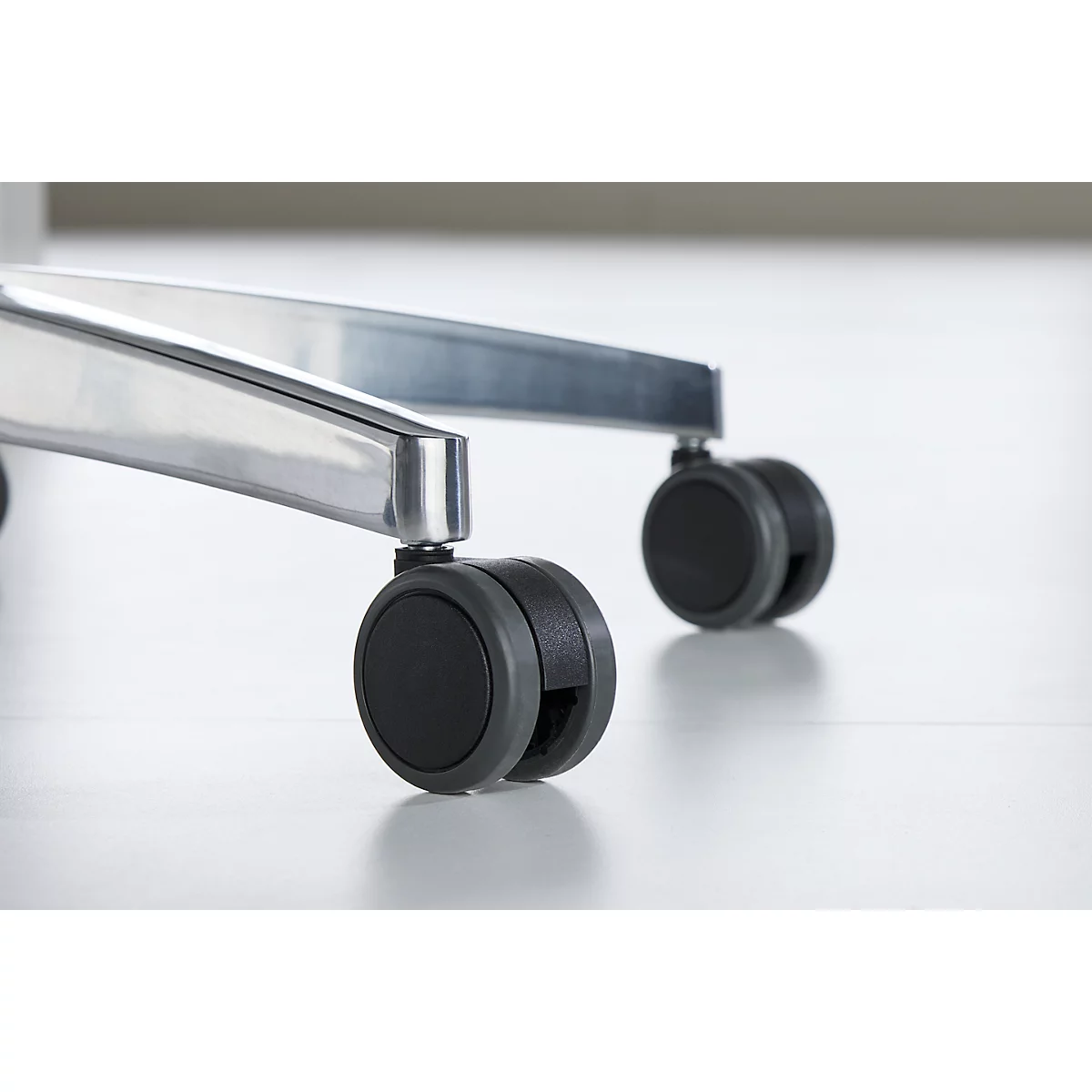 Close-up of an office chair: Detail view of the black casters and the silver frame on a light background.