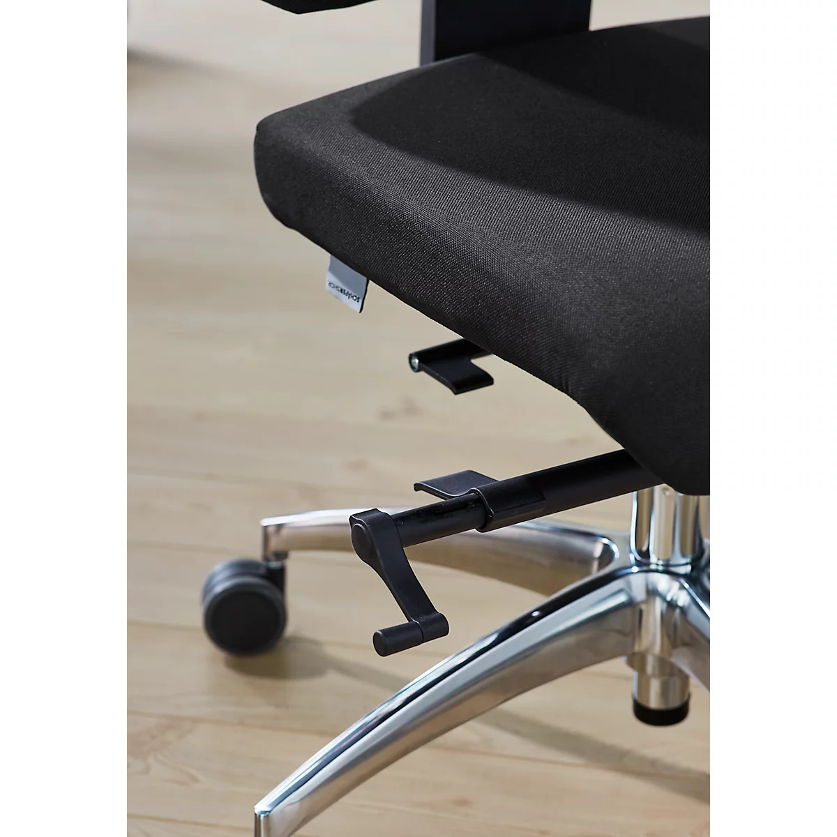 Close-up of a black office chair. The seat and backrest are made of fabric, the frame is metal. There are adjustment levers on the chair.