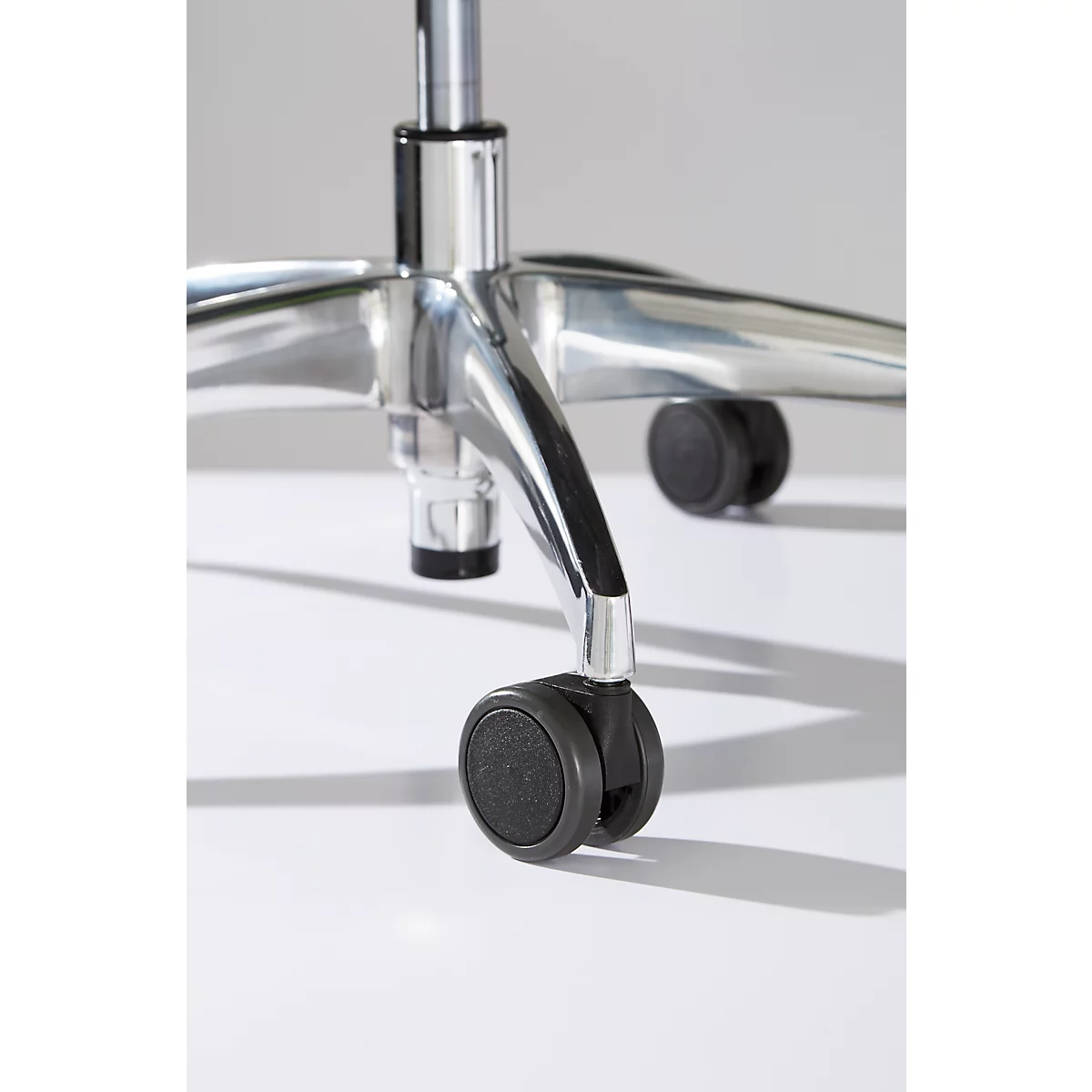 Close-up of the wheels and foot of an office chair, made of chrome-plated metal and black wheels. The image has a white background.