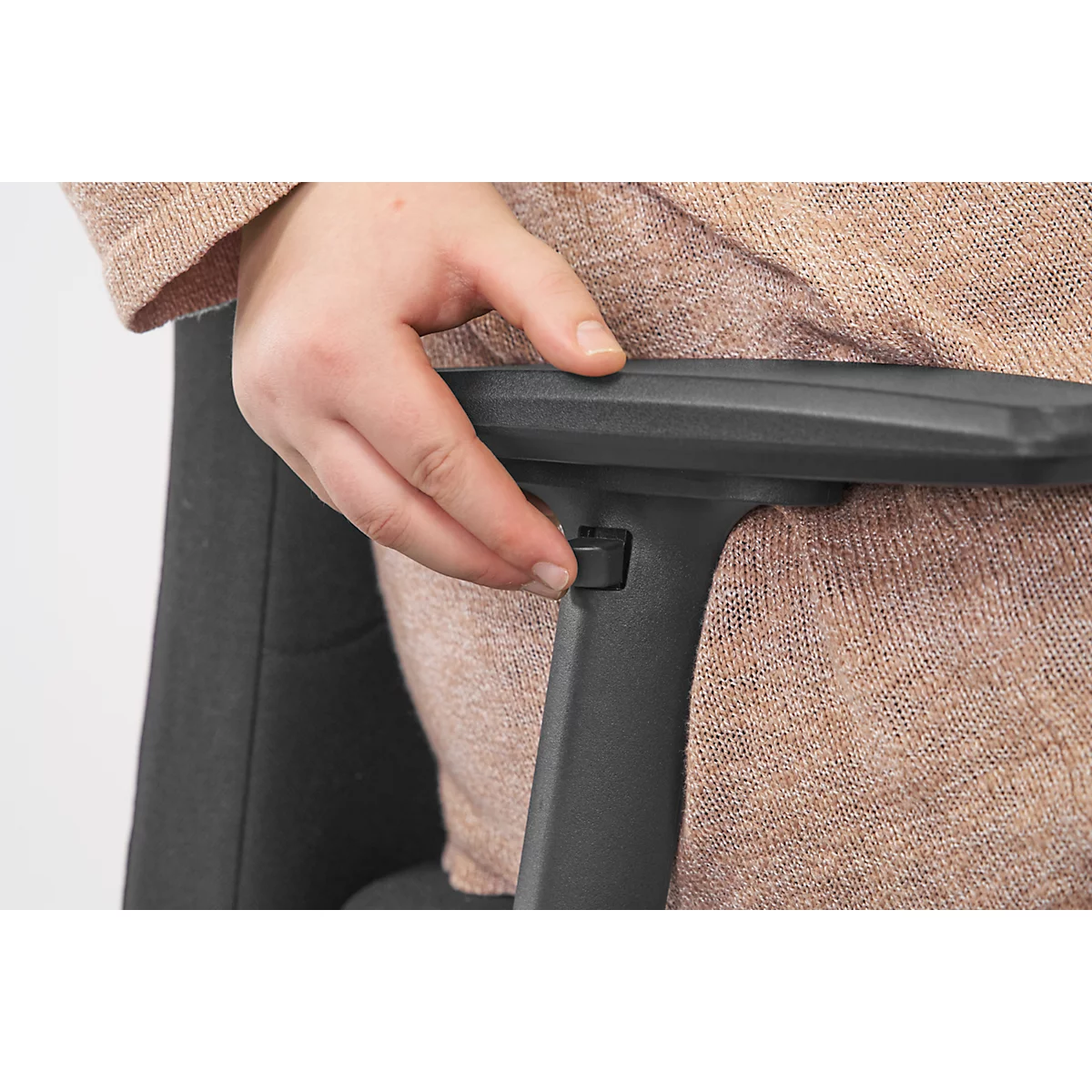 Close-up of a hand operating a button on the arm of a black office chair, against a background of brown clothing.