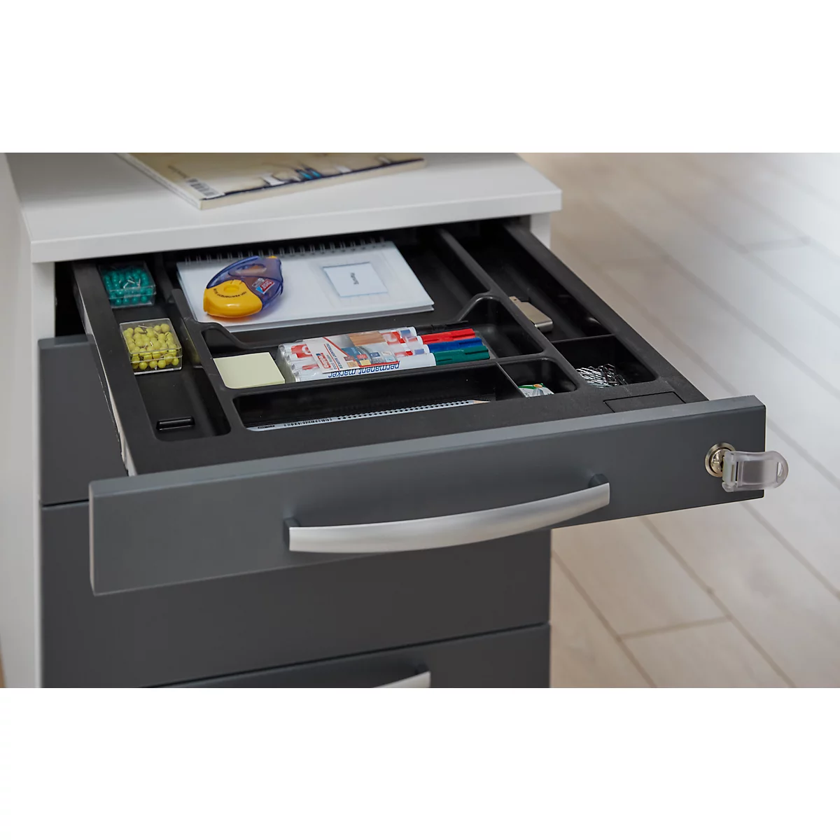 Gray filing cabinet with open drawer, filled with office supplies. Silver handle and lock.
