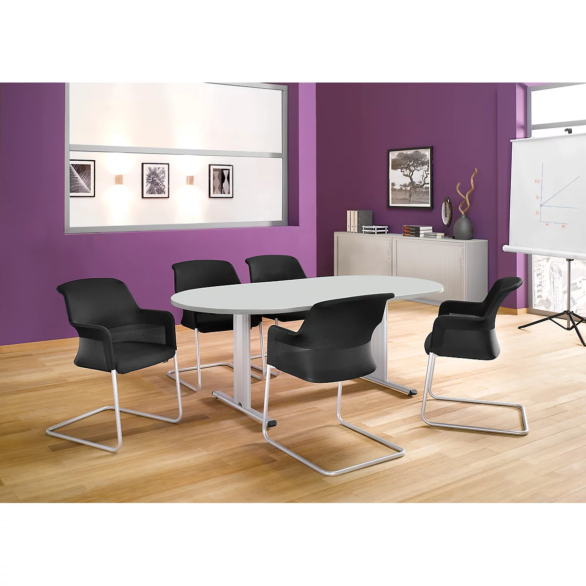 A conference room with an oval table, black chairs, and a flip chart.