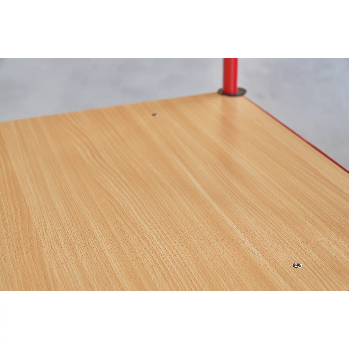 Close-up van een tafelblad met houtnerf. Rode poot van een tafel rechtsboven.