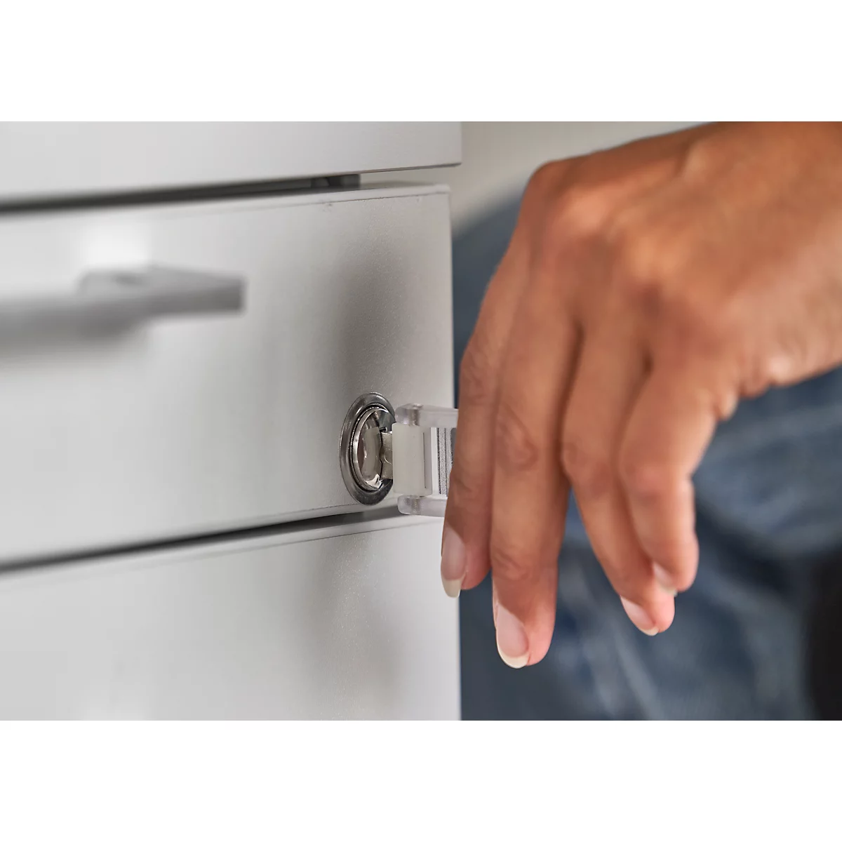 Hand öffnet eine Schublade an einem weißen Schrank. Das Schloss ist im Fokus.