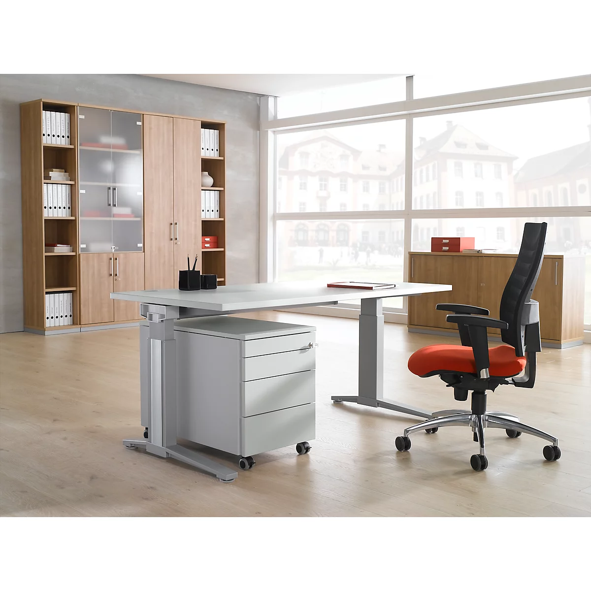 Büro mit Schreibtisch, Schrankwand und Bürostuhl. Ein Fenster zeigt eine Stadtansicht. Der Stuhl hat eine rote Sitzfläche.